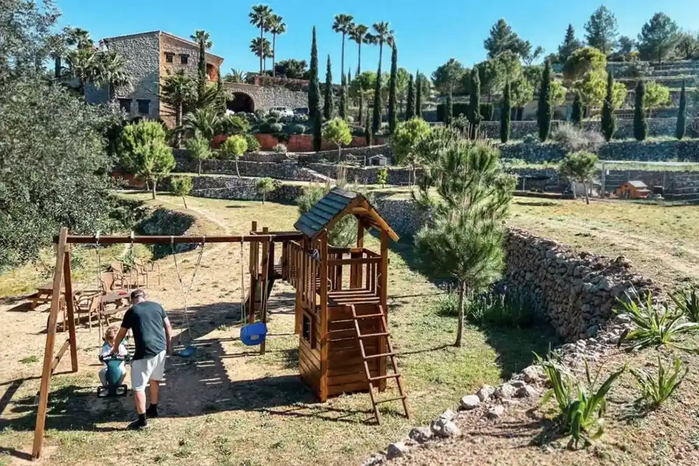 Small countryside hotel with an outdoor play area in Spain?, Dad pushes toddler on swing with a view of the hotel in the background